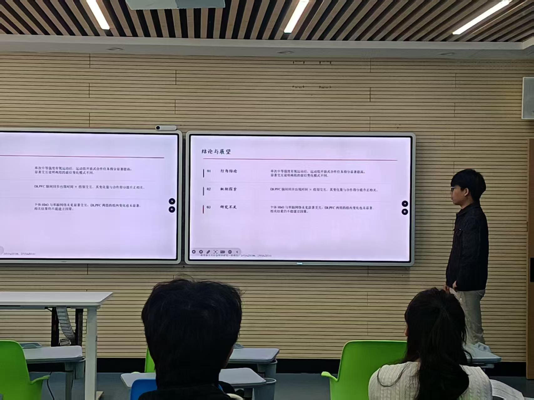 A conference speaker beside two screens showing the discussion and outlook slide
